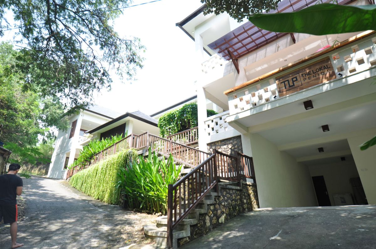 Modern tropical villa with white walls, wooden stairs, and lush greenery on a hillside path. - Bali Villas